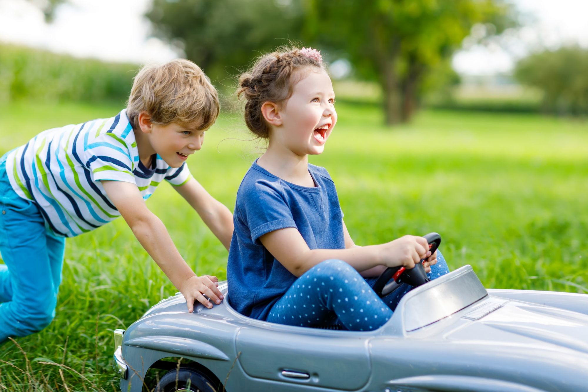 Zwei Kinder haben Spaß beim Spielen, ein Junge schiebt ein Mädchen im Auto an